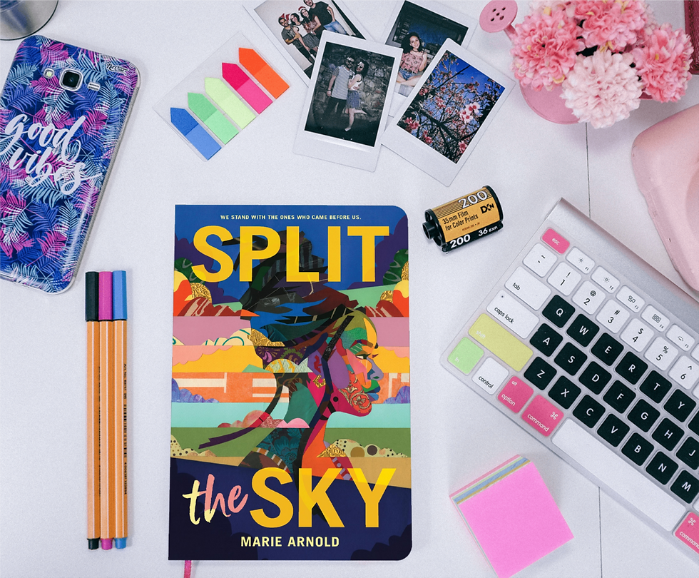 Book "Split the Sky" by Marie Arnold on a desk next to pictures, pencils, phone and keyboard.