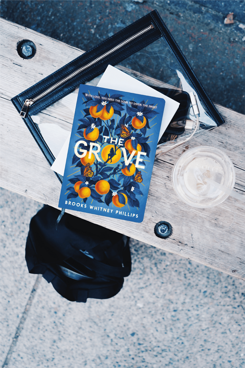 Book "The Grove" on a bench with clear bag and water next to it.