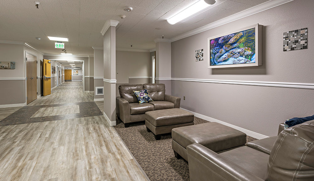 A warm, cream and khaki-colored hallway, extending vertically towards the back of the building. This hallway also has beige leather couches and ottomans placed along the right-hand side of the hallway facing each other with a large coral reef painting hanging in the middle.