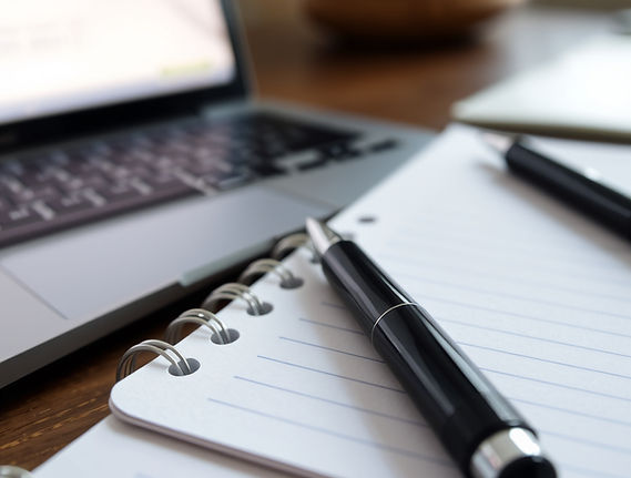Close-up of a pen lying on a notepad with a laptop in the background.jpg