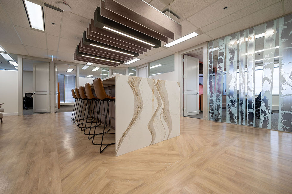 Modern office lounge with brown bar stools around a marble island, wood floors, glass walls, and sleek pendant lights.
