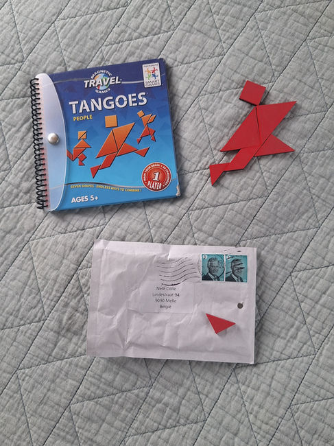 Tangoes spel met rood mannetje naar het boekje op grijsgroene sprei met onder het boekje en mannetje een enveloppe met een ontbrekende stukje van het mannetje
