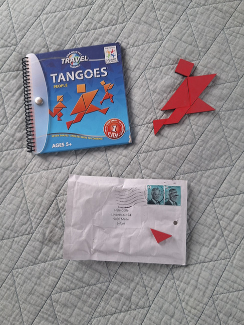 Tangoes spel met rood mannetje naar het boekje op grijsgroene sprei met onder het boekje en mannetje een enveloppe met een ontbrekende stukje van het mannetje