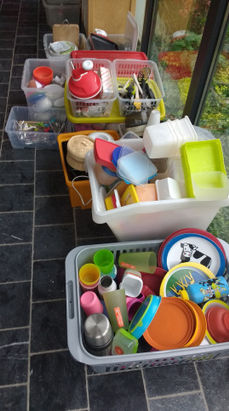 Diverse plastic bakken met keukengerei en servies op donkere tegels.