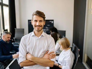 Smiling businessman standing confidently with arms crossed in an office setting.