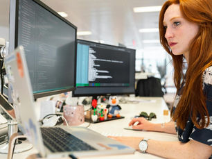A focused female software engineer coding on dual monitors in a modern office.