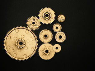Close-up of golden gears and cogs arranged on a black background, representing teamwork and industry.