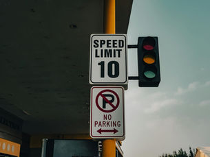 Close-up of a speed limit sign and traffic lights at an intersection under a cloudy sky.