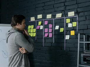 Adult male focusing on task planning using sticky notes on a black wall in a contemporary office setting.