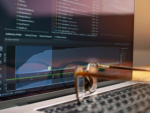 Laptop screen displaying code and performance graphs with eyeglasses resting on the keyboard.