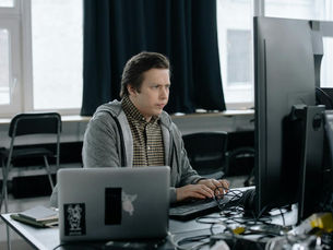 A dedicated programmer focused on coding at his workspace with dual monitors in a modern office setting.
