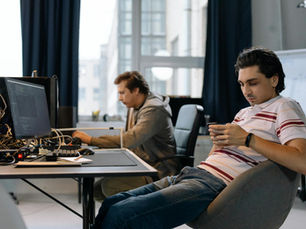 Two men working in a modern office, one on a computer and the other on a smartphone.