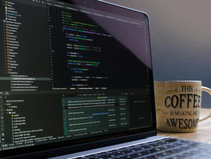 Close-up of laptop with coding software and a motivational coffee mug on a desk.