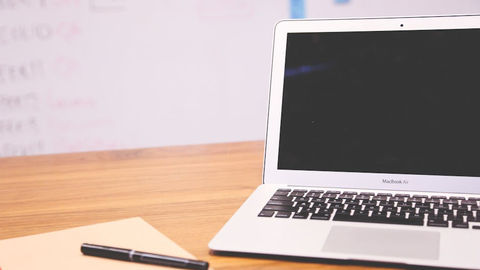 Sleek laptop on wooden desk with pen and notepad.