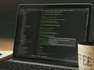 A close-up of a laptop displaying code in a dimly lit room with a coffee mug nearby.