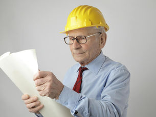 Thoughtful aged male contractor wearing formal shirt and construction helmet examining paper draft