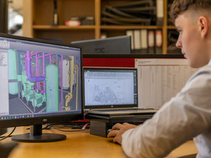 Engineer working with CAD software on dual monitors in an office setting.