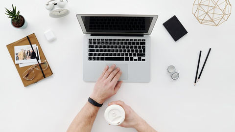 Top view of a minimalist desk with laptop, coffee cup, and office supplies.