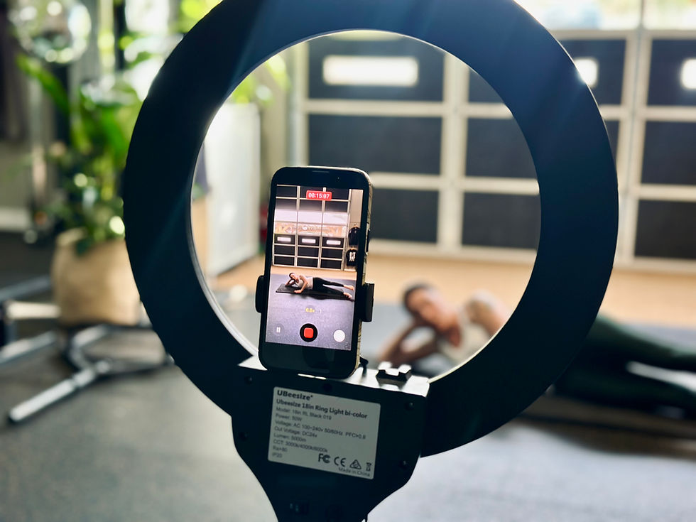 Smartphone on a ring light records a woman doing floor exercises in a bright studio; timer 00:15:07 glows on screen.
