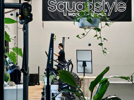 Person exercises on a cardio machine in a plant-filled gym, under a Squadstyle workout banner.