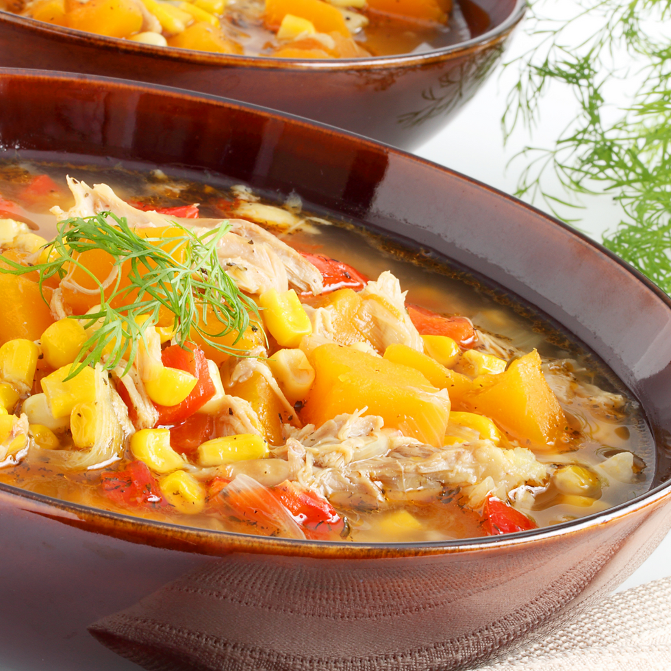 A bowl of shredded chicken with various vegetables including squash and corn