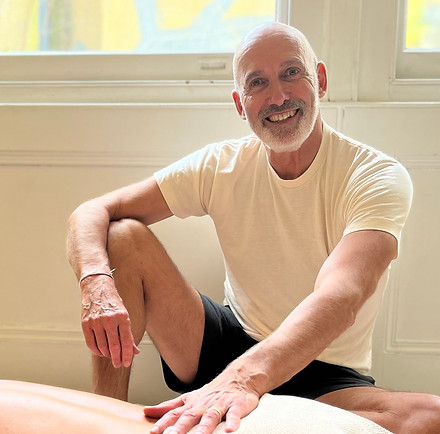 Martin Feaver smiling looking towards the camera. He is wearing a cream t shirt and green shorts. His hand is resting on the back of a client.