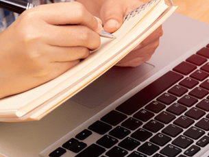 A person takes notes on a paper while completing management training programs online