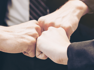 Three people on a team fist bumping, a healthy behavior indicating corporate wellness