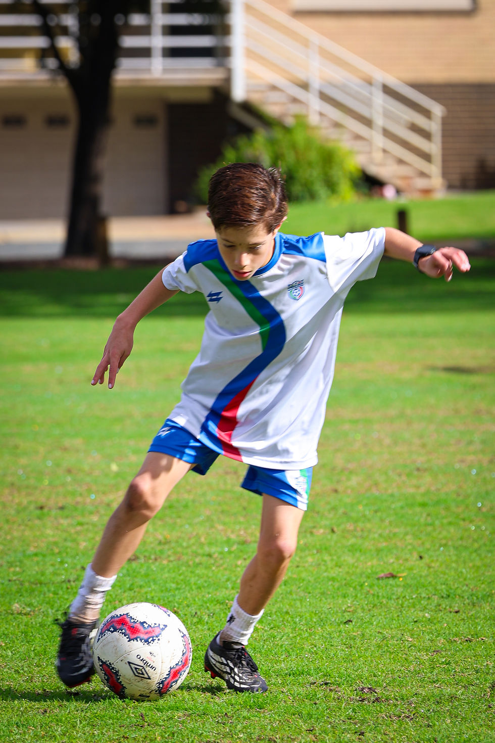 A young soccer player performing close-control dribbling drills in a small grass backyard in Perth