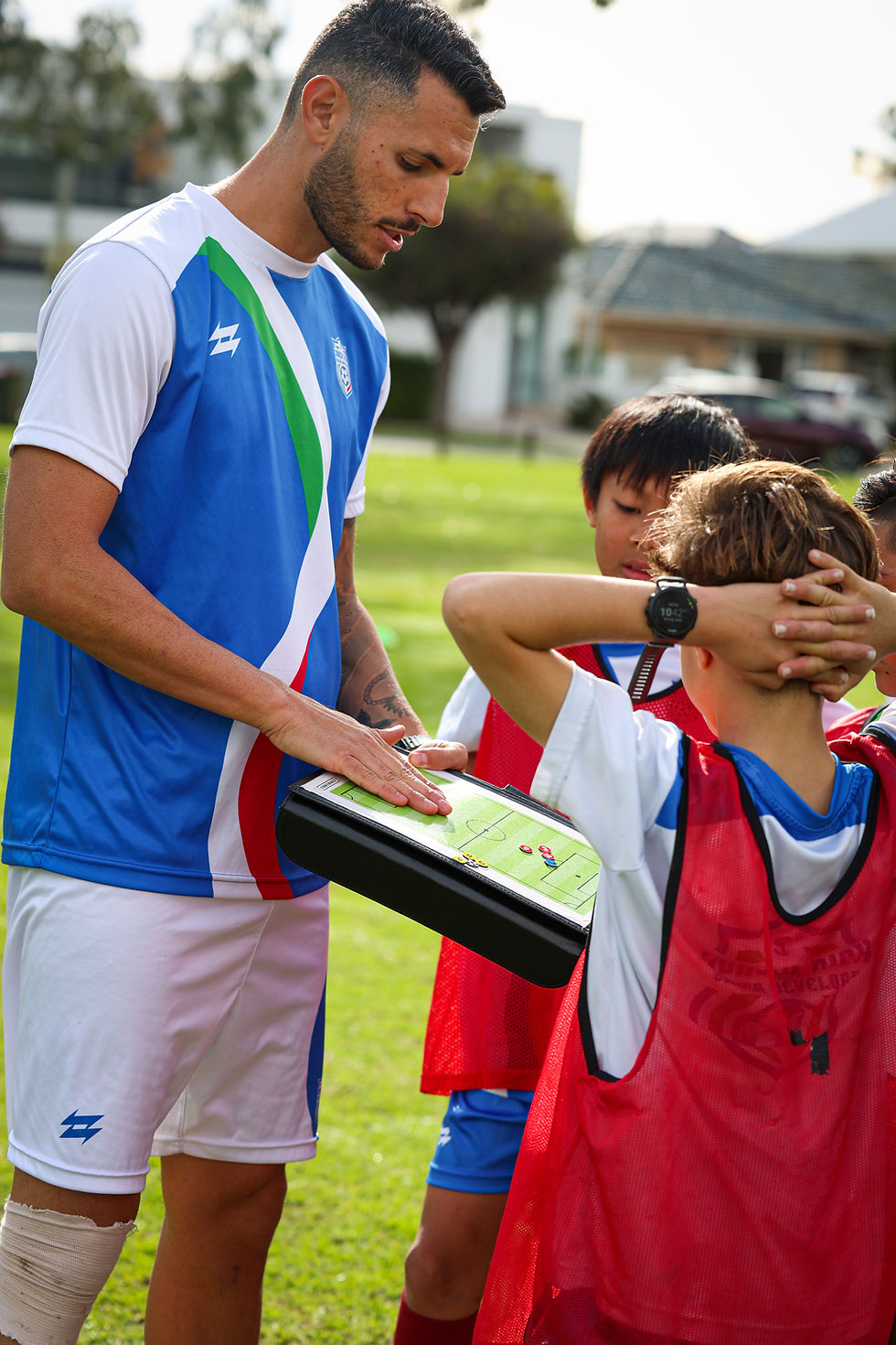 Coach Nick explains match strategies to young players using a tactical board during a training session.