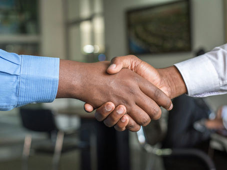 Close-up of two men shaking hands in an office, one in a blue shirt and one in white, suggesting agreement and trust