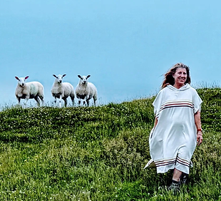 Lara Long, LPC, walking along a grassy hillside while three curious sheep look on.