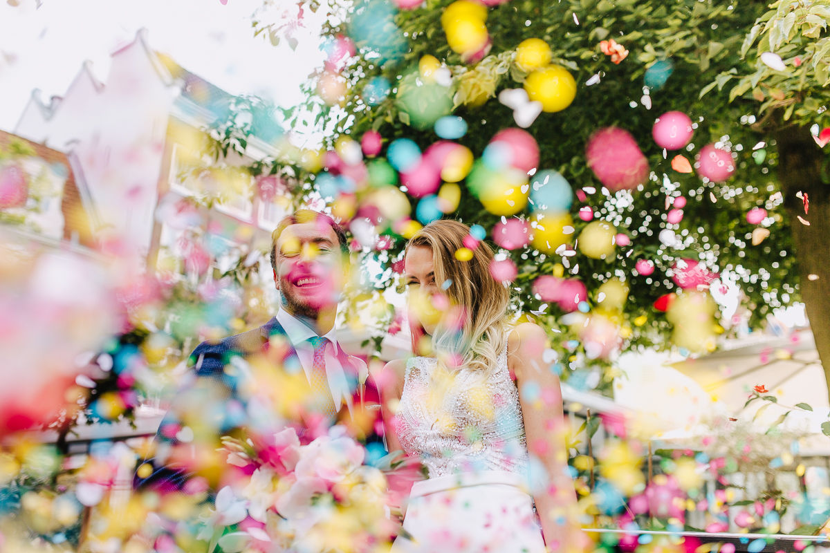 a bride and groom are almost not visible through a storm of colorful confetti