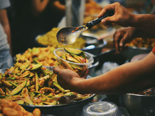 Hands serve spicy green mango pickle into a plastic bowl at a vibrant street food stall. Bright green and red hues.