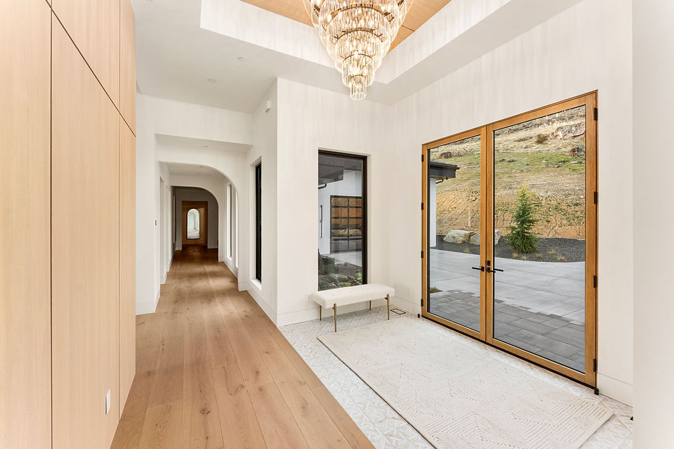 Spacious hallway with light wood floors, elegant chandelier, and large glass doors revealing a scenic outdoor view. Minimalist decor.