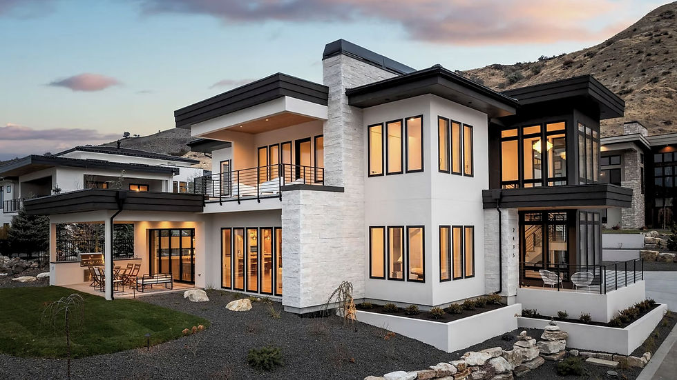 Modern two-story house with large windows and balcony at sunset, surrounded by hills. Warm interior lights illuminate the sleek design.
