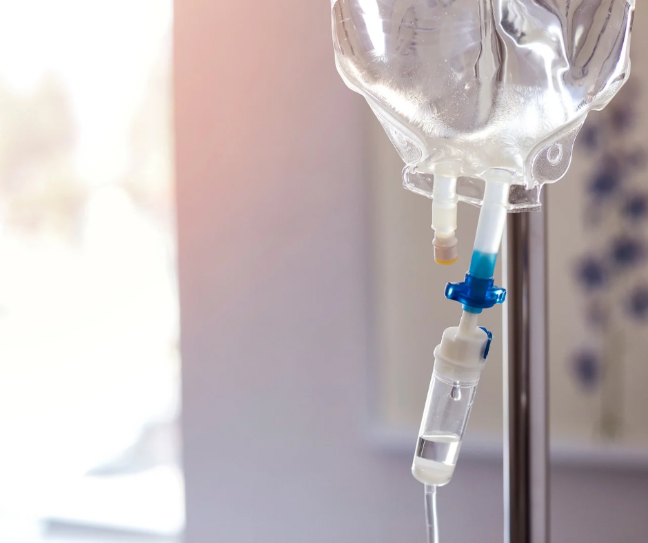 Close-up of an IV drip bottle containing blue liquid with air bubbles, set against a soft turquoise background, evoking a calm, clinical mood.