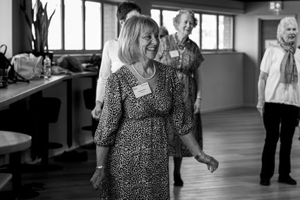 Smiling woman walking indoors with others in background.
