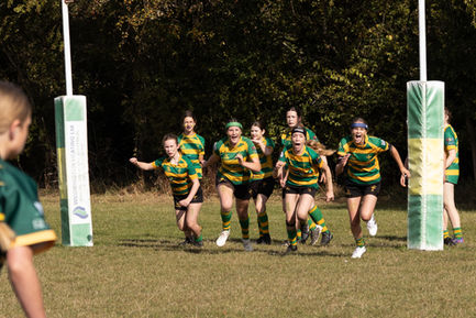 Women in green and yellow rugby uniforms running.