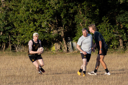 Three people playing rugby on a grassy field.