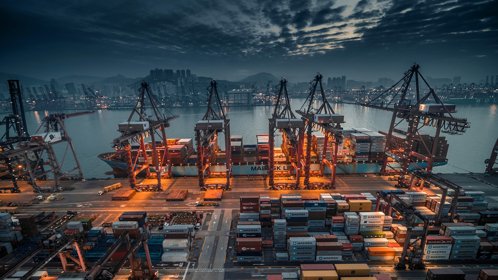 Container ship being loaded by cranes at a busy Asian port at dusk