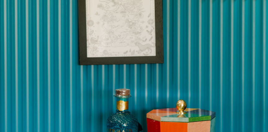 Colourful ice bucket with gin bottle beside it and wall pictures above