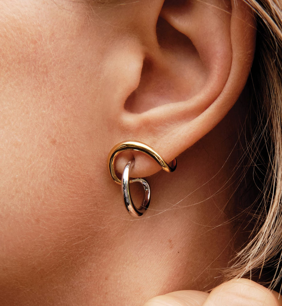 Two-tone sculptural stud earrings worn on an ear