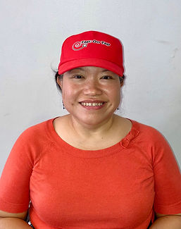 Puspa Poarangan. She is an olive-skinned adult woman with dark brown hair. She is in a wheelchair. She is wearing a red hat that says Tap: On Tap. She is wearing an orange short-sleeved shirt.