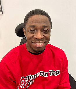 Blake Hunt. He is a dark-skinned adult man with black hair. He is in a wheelchair. He is wearing a red long-sleeved shirt that says Tap: On Tap.