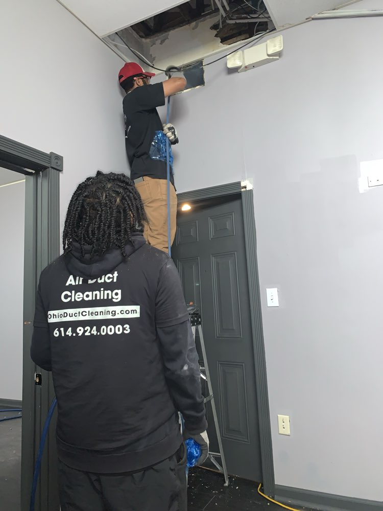 Clean Air Pros technician on ladder cleaning ductwork in a Columbus Ohio medical office — safety-first protocol
