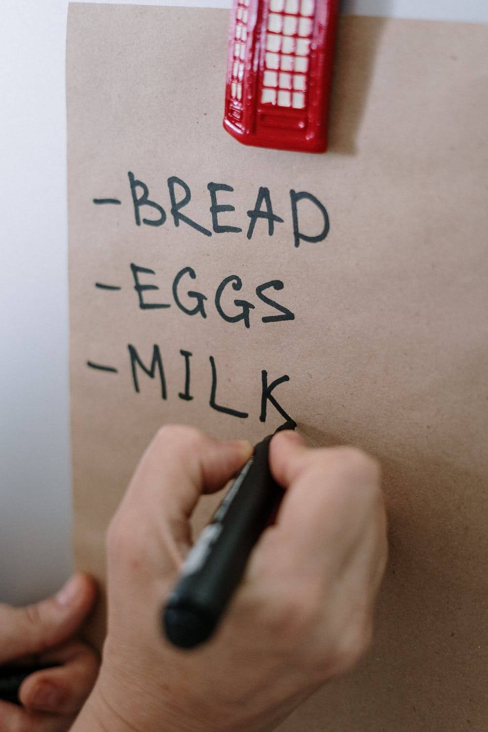 A person writing a shopping list which consists of bread, eggs and milk