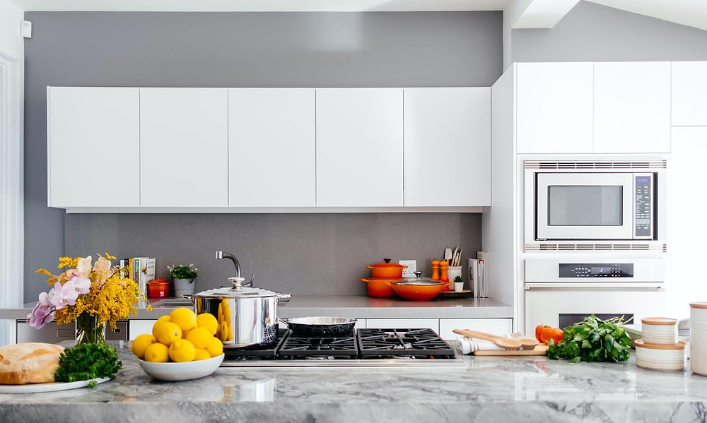 A white kitchen with fruits, pots, pans, flowers, books and cutlery all arranged aesthetically
