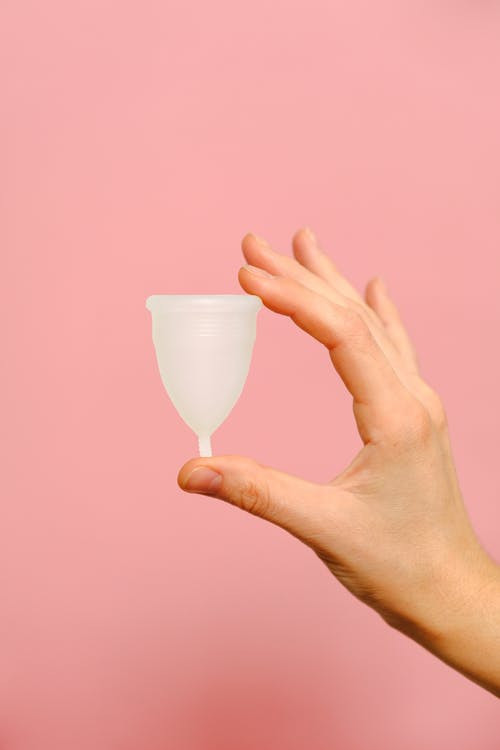 Seseorang memegang menstrual cup berwarna putih di depan latar belakang merah muda