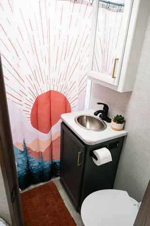 A bright, clean bathroom with sleek, modern finishes; a fun shower curtain featuring a colorful design of the sun rising above mountain peaks adds a cheerful, artistic touch to the space.







